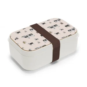 Whimsical hand-drawn black and white cows in black, white, and grey on a pale pink background, featured on a practical bento lunchbox with a natural wood lid. The design combines charm and functionality for on-the-go meals.