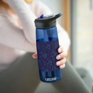 A woman wearing a soft pink jumper and grey leggings sits near a window, holding a blue CamelBak water bottle close to the camera, with light streaming in.