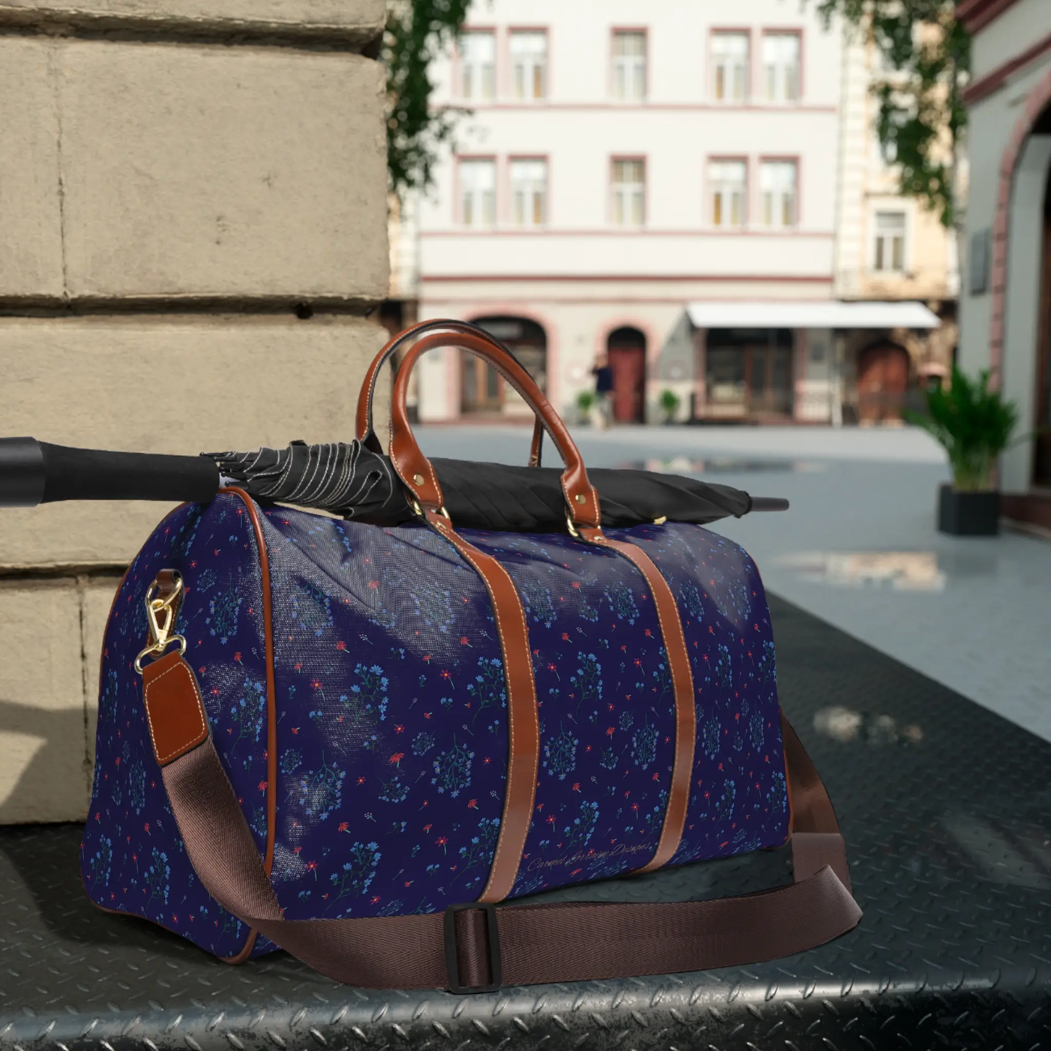Woodland Bloom travel bag featuring a deep navy floral pattern with lilac, saffron, magenta, and periwinkle wildflowers, finished with brown PU leather handles and a gold zipper.